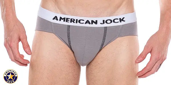 Men's gray bikini underwear with a white waistband featuring 'AMERICAN JOCK' logo made from soft material shown on a model