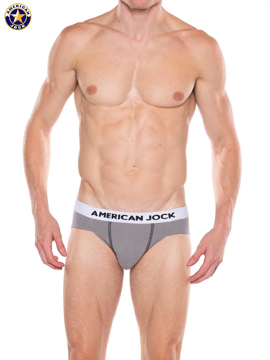 Men's bikini underwear in platinum gray with a contrasting waistband featuring the brand name American Jock worn by a model