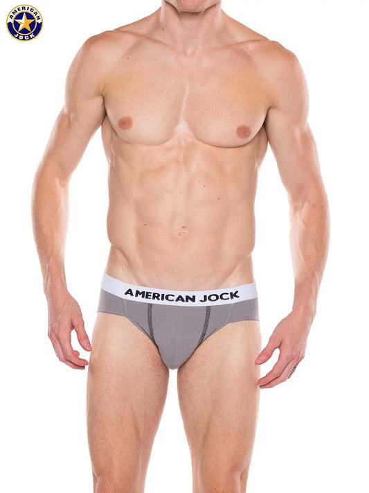 Men's bikini underwear in platinum gray with a contrasting waistband featuring the brand name American Jock worn by a model