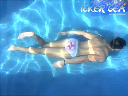 A man floats underwater wearing icker sea lifeguard micro slip bikini swimwear white with a red cross emblem