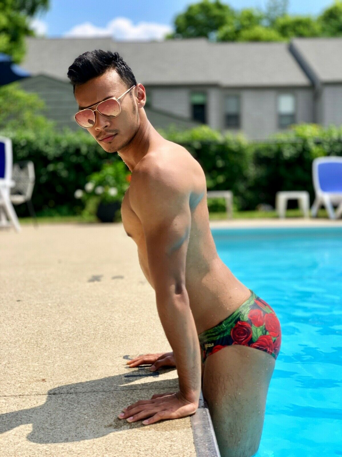 Men's swim briefs in red with rose print made by Maris Equi shown on a model by a poolside.