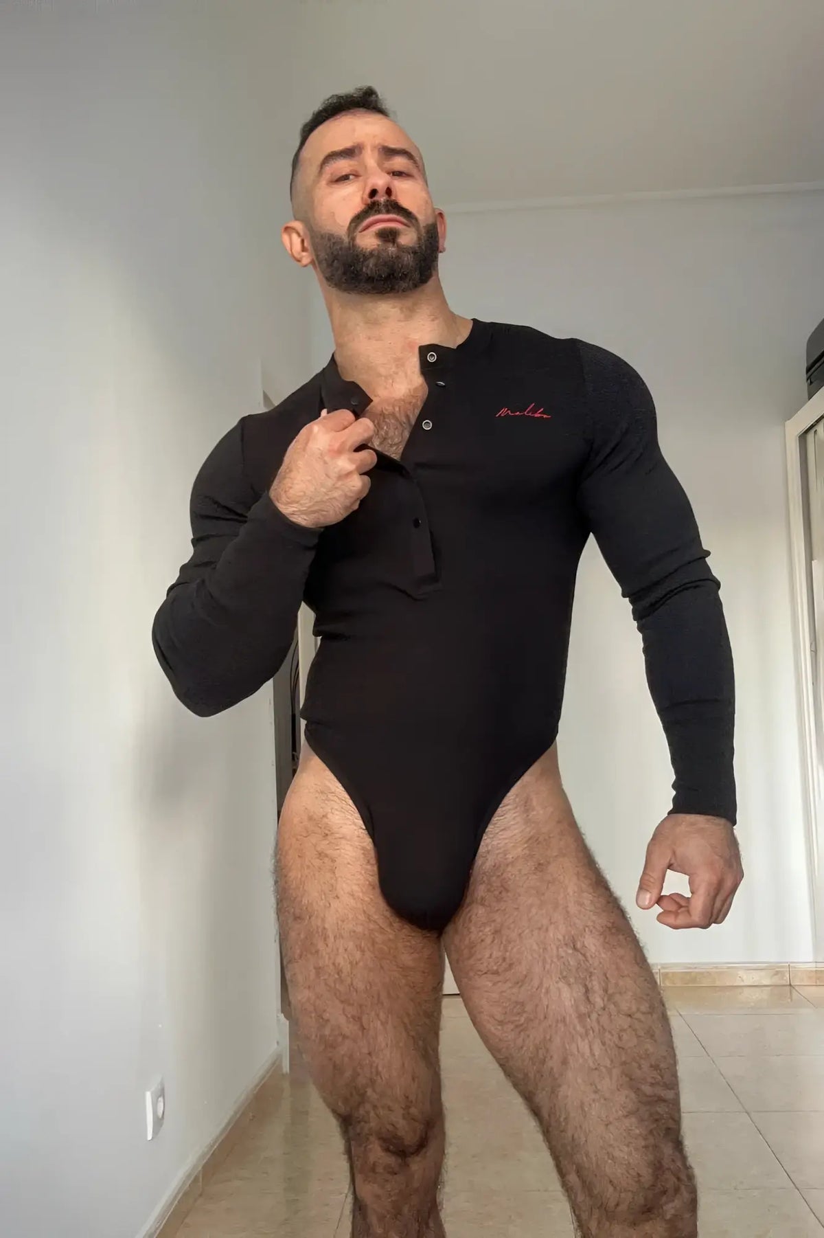 Black long sleeve infinity bodysuit with buttoned front and subtle red embroidery on the chest in midnight black