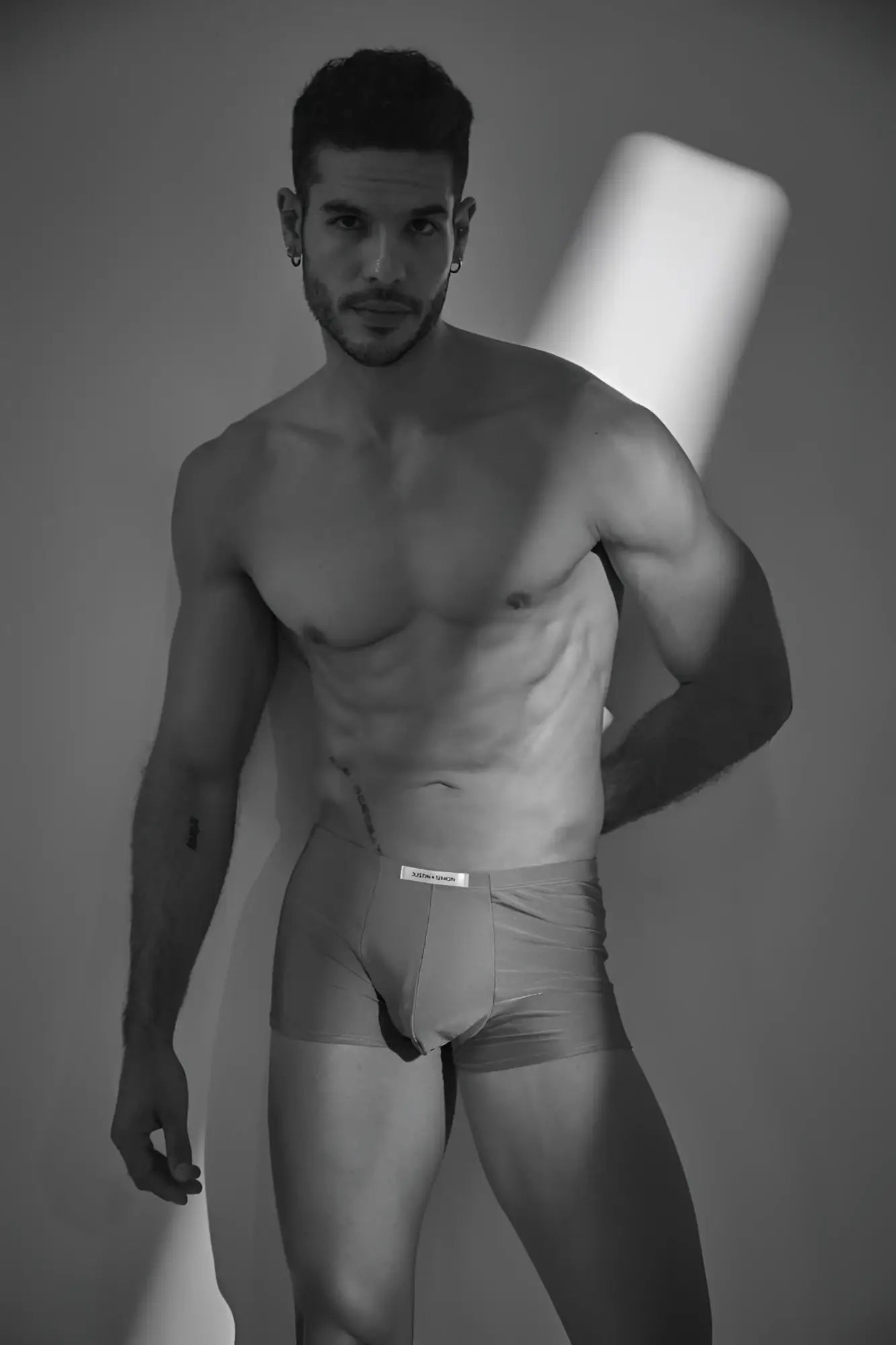 A man wearing light-colored form-fitting calvin klein classic boxer briefs with a metal green waistband label