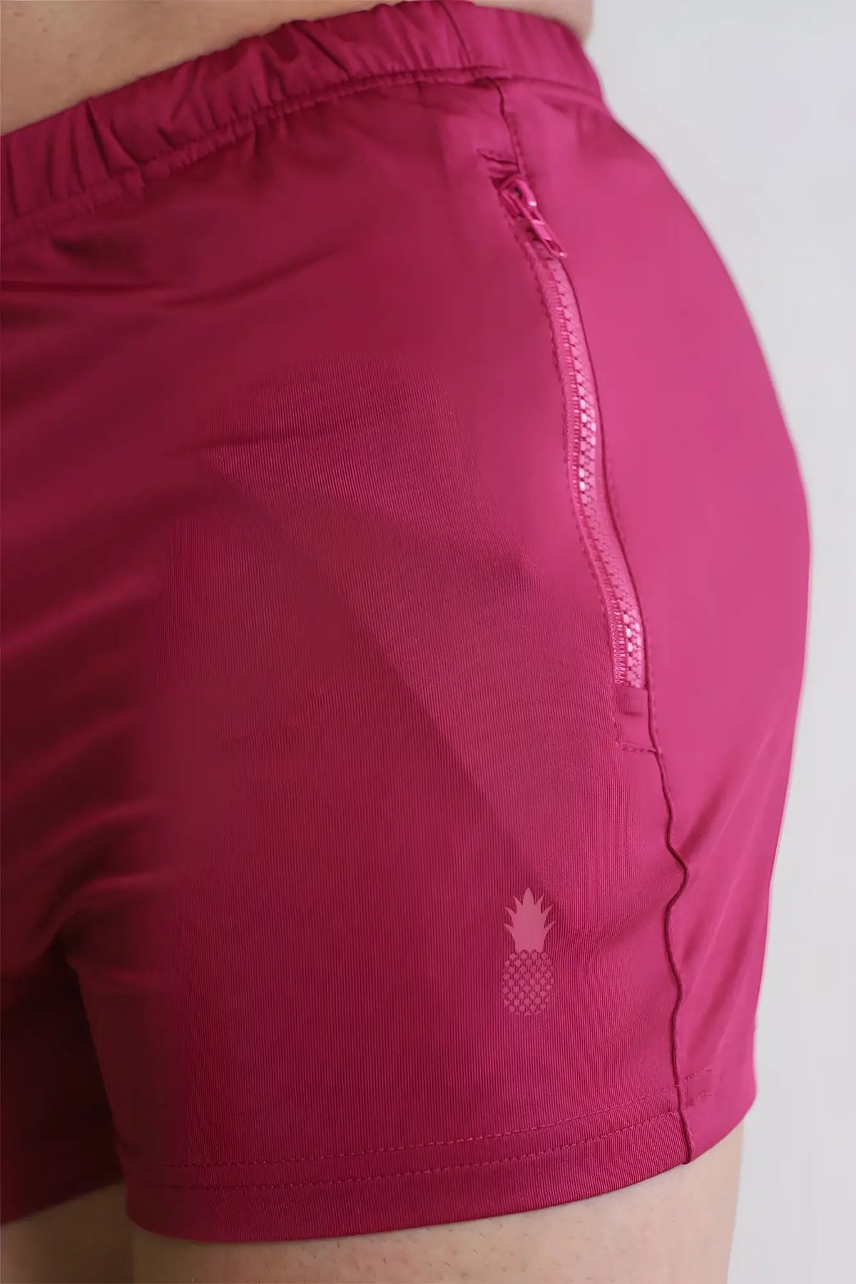 Magenta fuchsia karma 2 inch short shorts with zipper pockets and a subtle pineapple logo on the lower leg