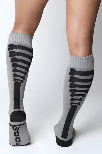 Gray kennel club bones knee high socks with black skeletal design and wood printed on the heel visible from the back