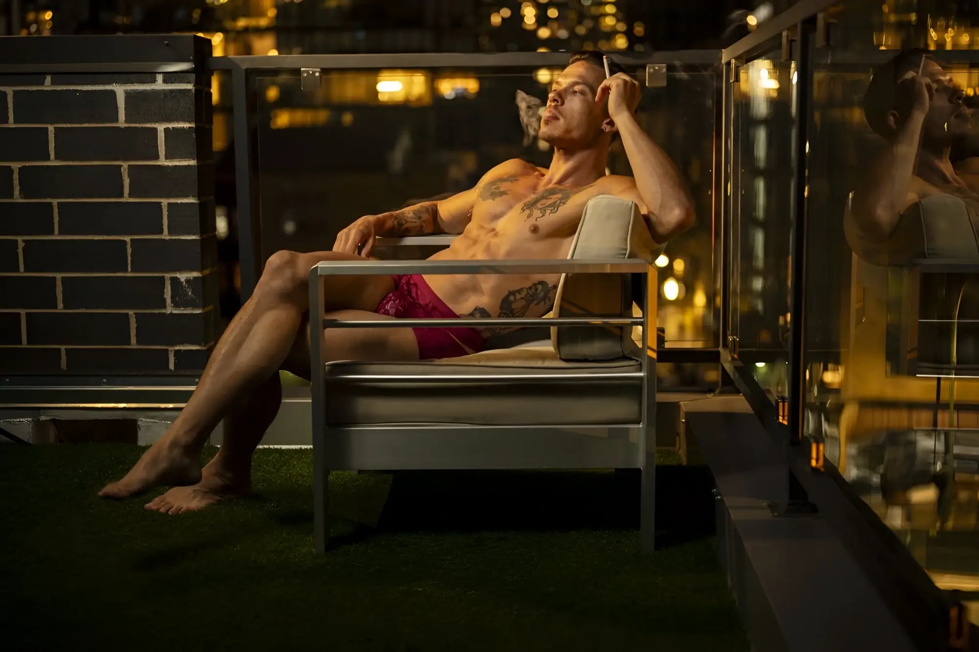 A man with tattoos lounges in a modern metal-framed chair wearing male power 126-289 lucifer cut out short burgundy