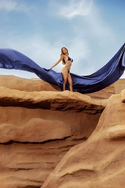 A woman stands on red rocks wearing a mapale 67158 deep ocean two piece swimsuit with flowing blue fabric