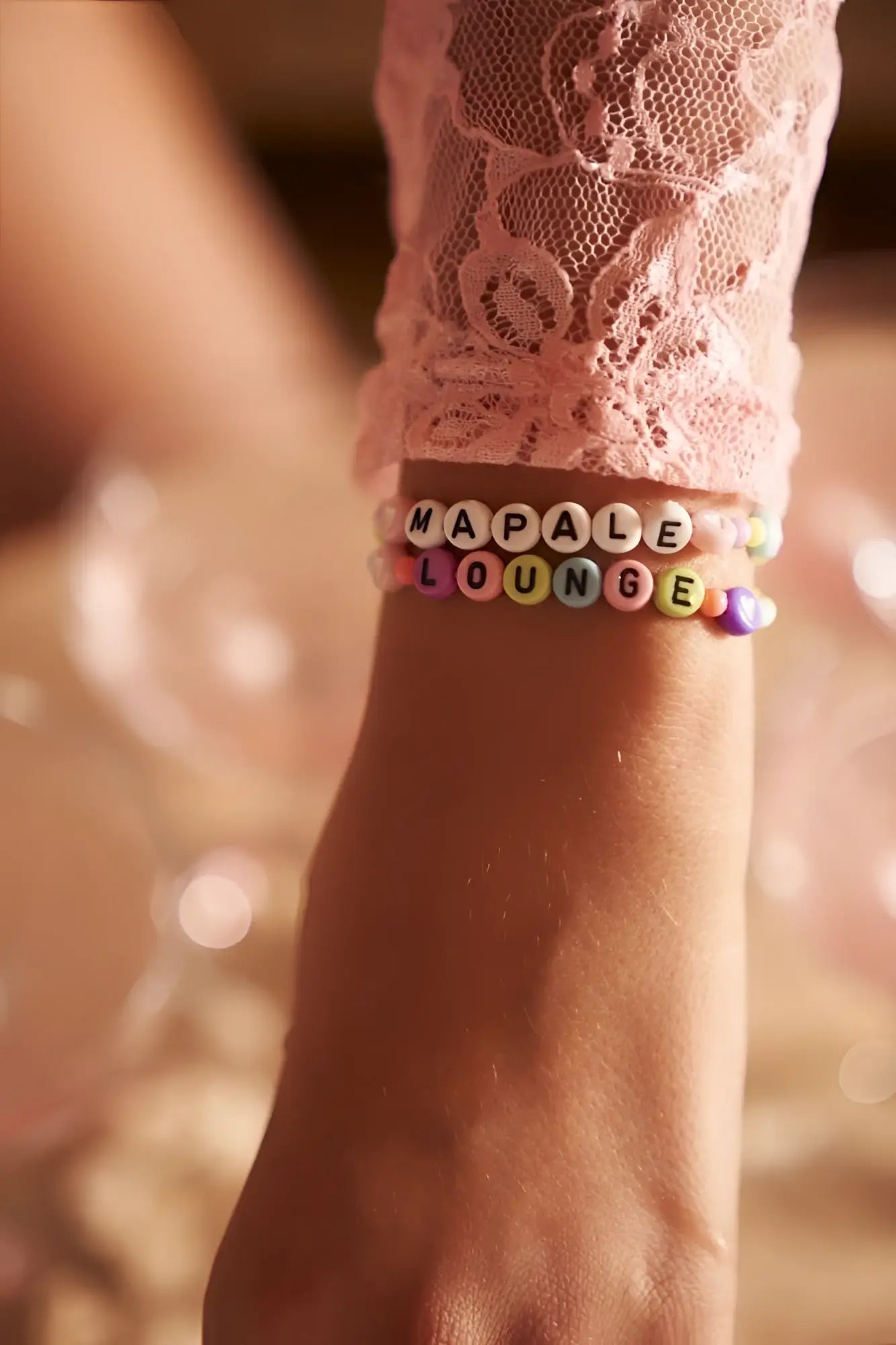 A colorful beaded bracelet with alphabet beads spelling mapale lounge worn on a wrist with mapale 7599 rose romper