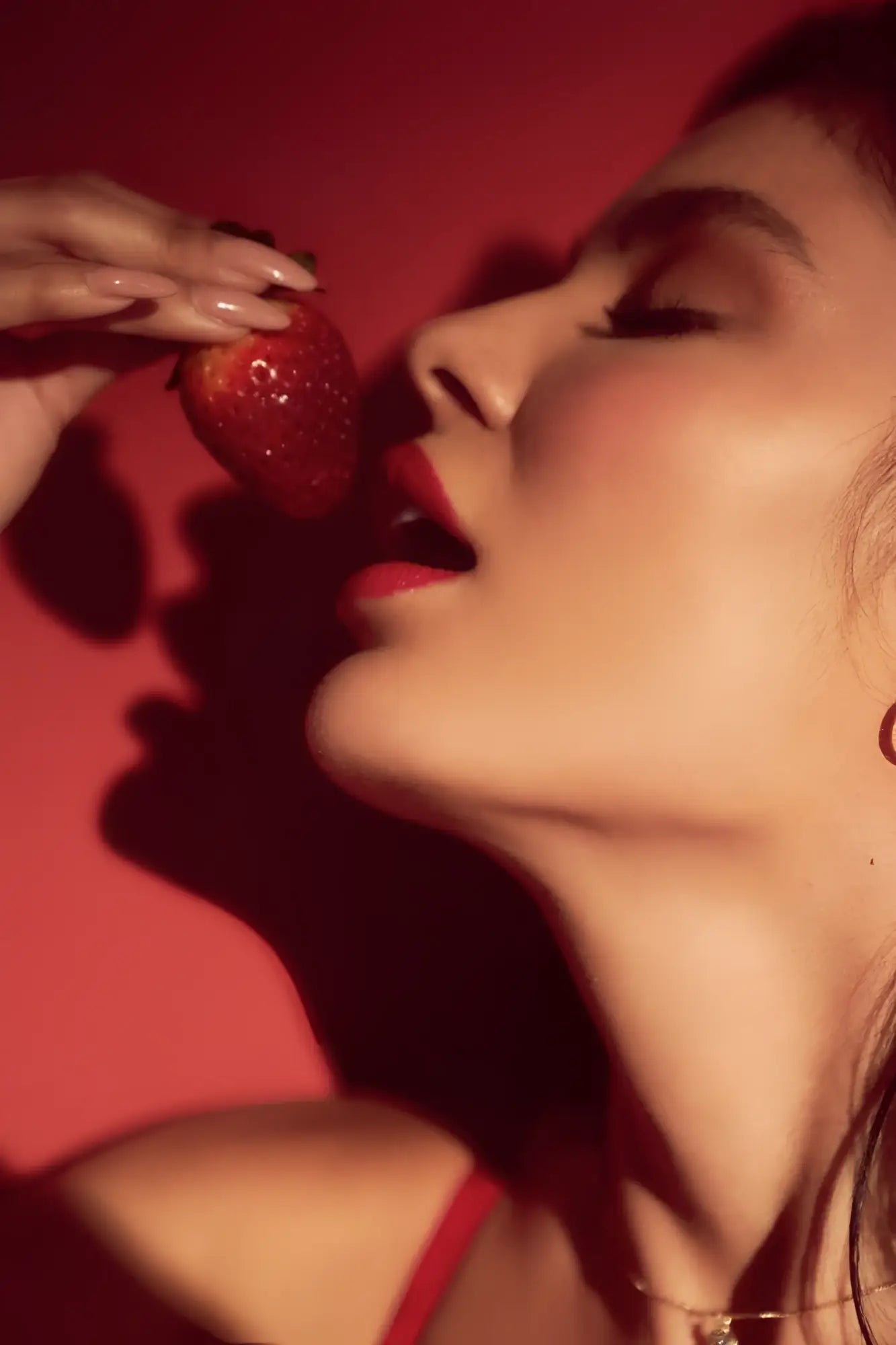 A ripe red strawberry held by a hand with manicured nails featuring the mapale 8899 black red two piece set