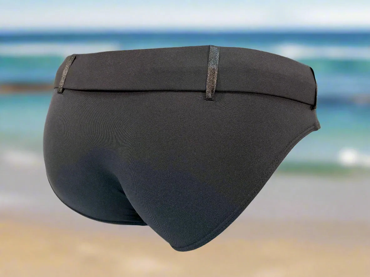 Black men's swim briefs by Maris Equi featuring a sleek design and elastic waistband shown against a beach background.