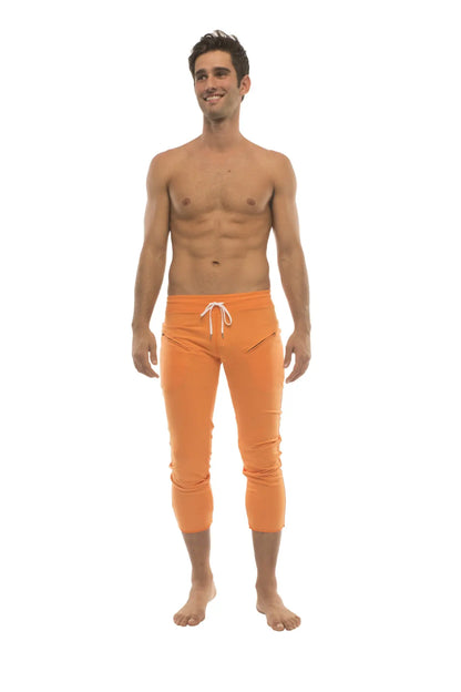 Mens solid orange capri yoga pants with white drawstring waistband and zipper pockets for athletic use