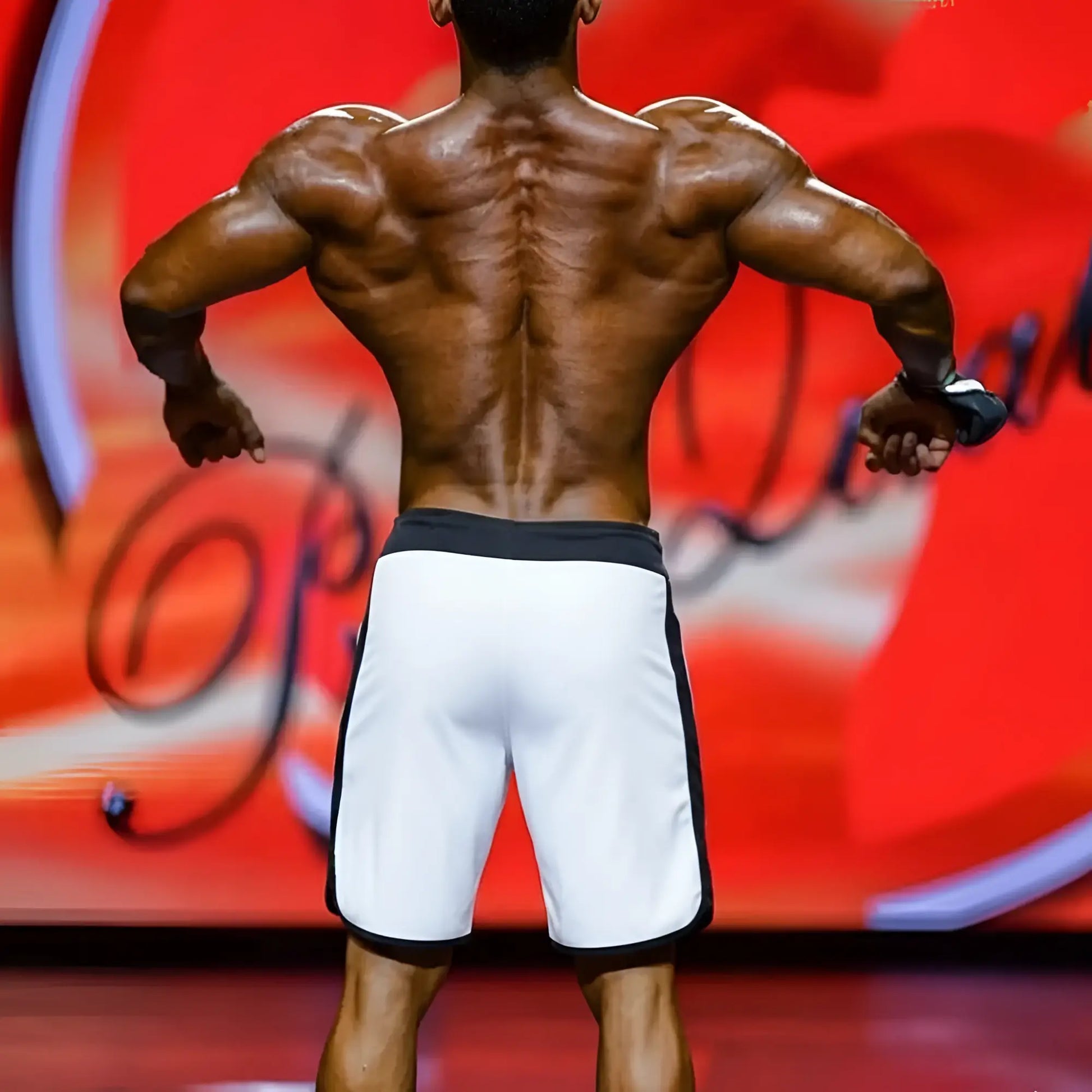 Back view of white board shorts with black trim on a muscular physique competitor.