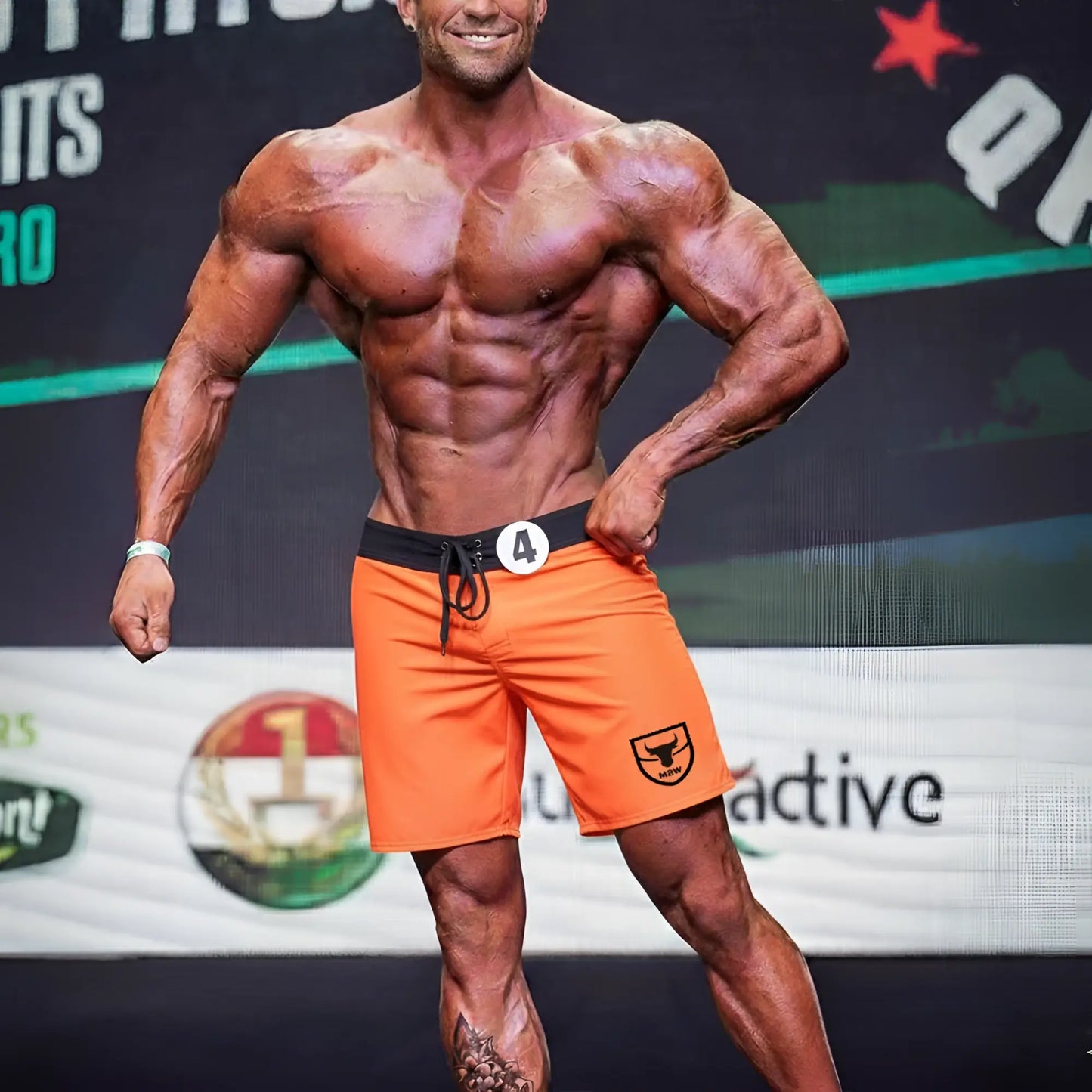 Orange athletic shorts with black waistband and drawstring featuring small shield logo on lower right leg from metromalewear