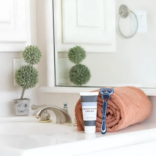 A blue and black disposable five-blade razor resting on a rolled terracotta towel with mixologie manscaping cream shave lotion sent iii