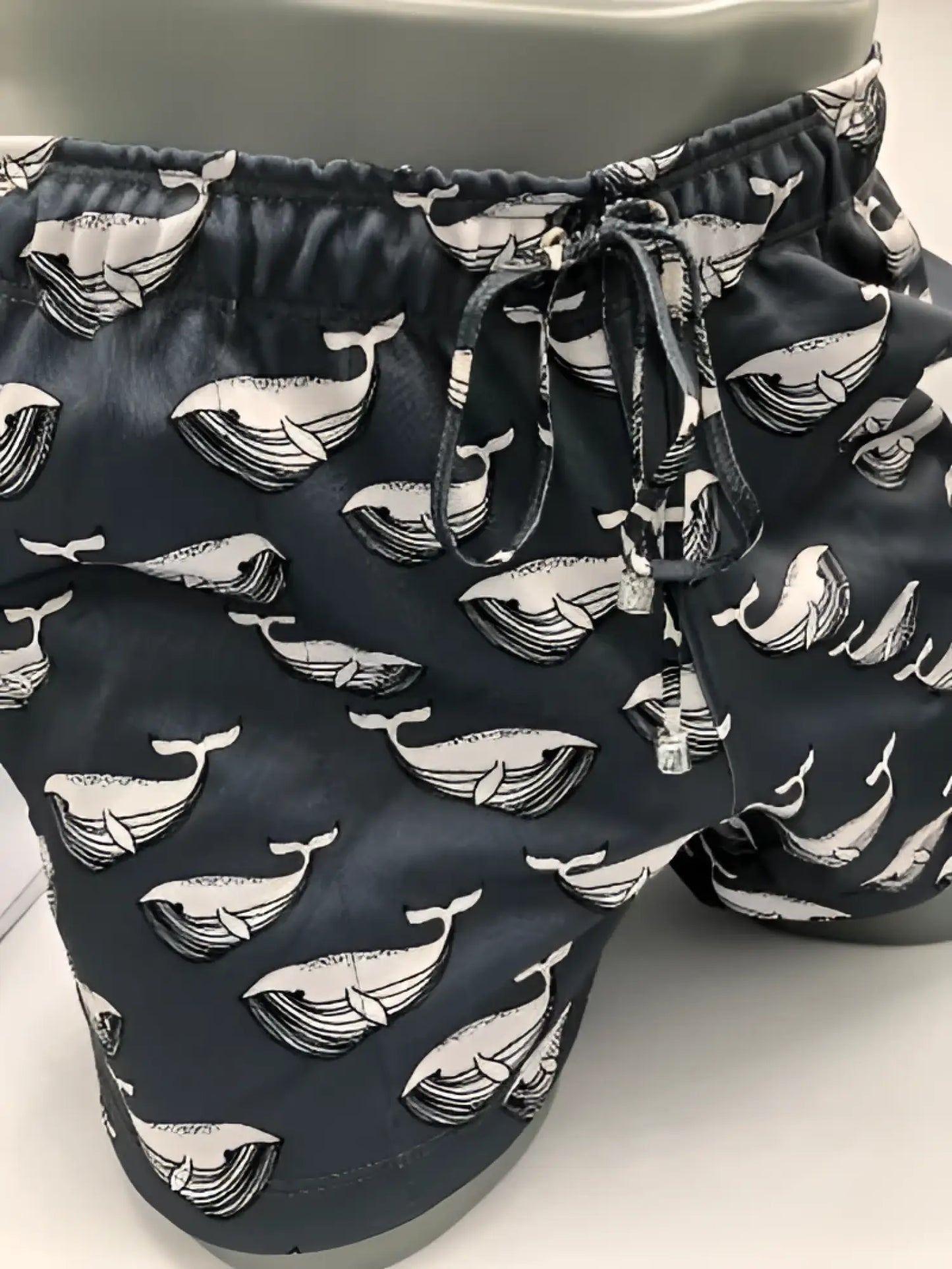 Black moby dick shorts with repeating white whale line art pattern made for swimwear use