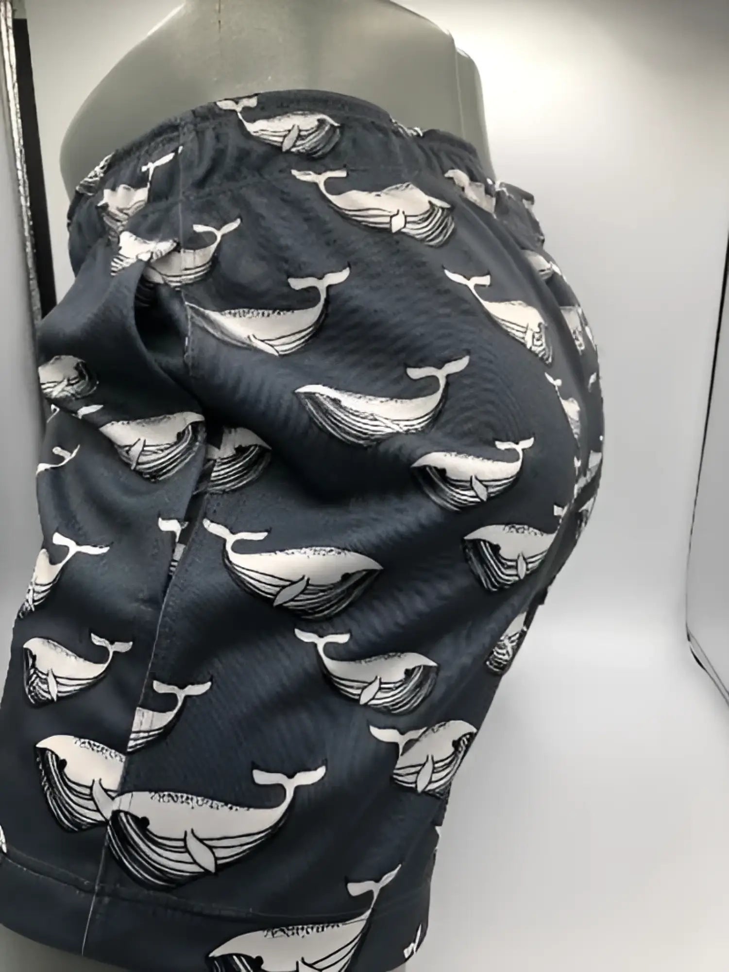 Dark gray moby dick shorts with a repeating white whale pattern ideal for swimwear and beach use