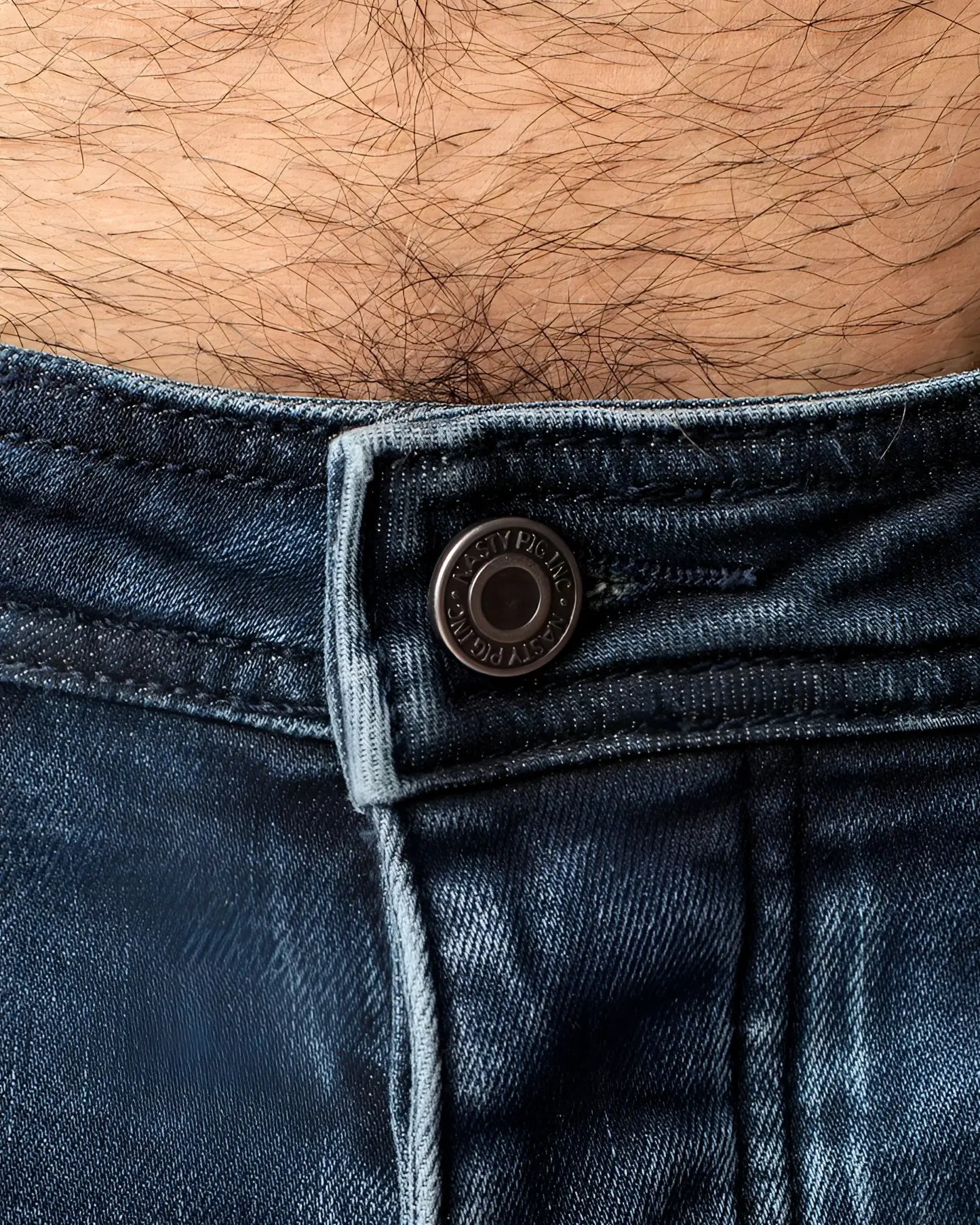 Dark blue denim np jean featuring a metallic button with embossed text on the front waistband