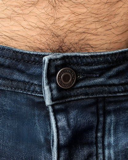 Dark blue denim np jean featuring a metallic button with embossed text on the front waistband