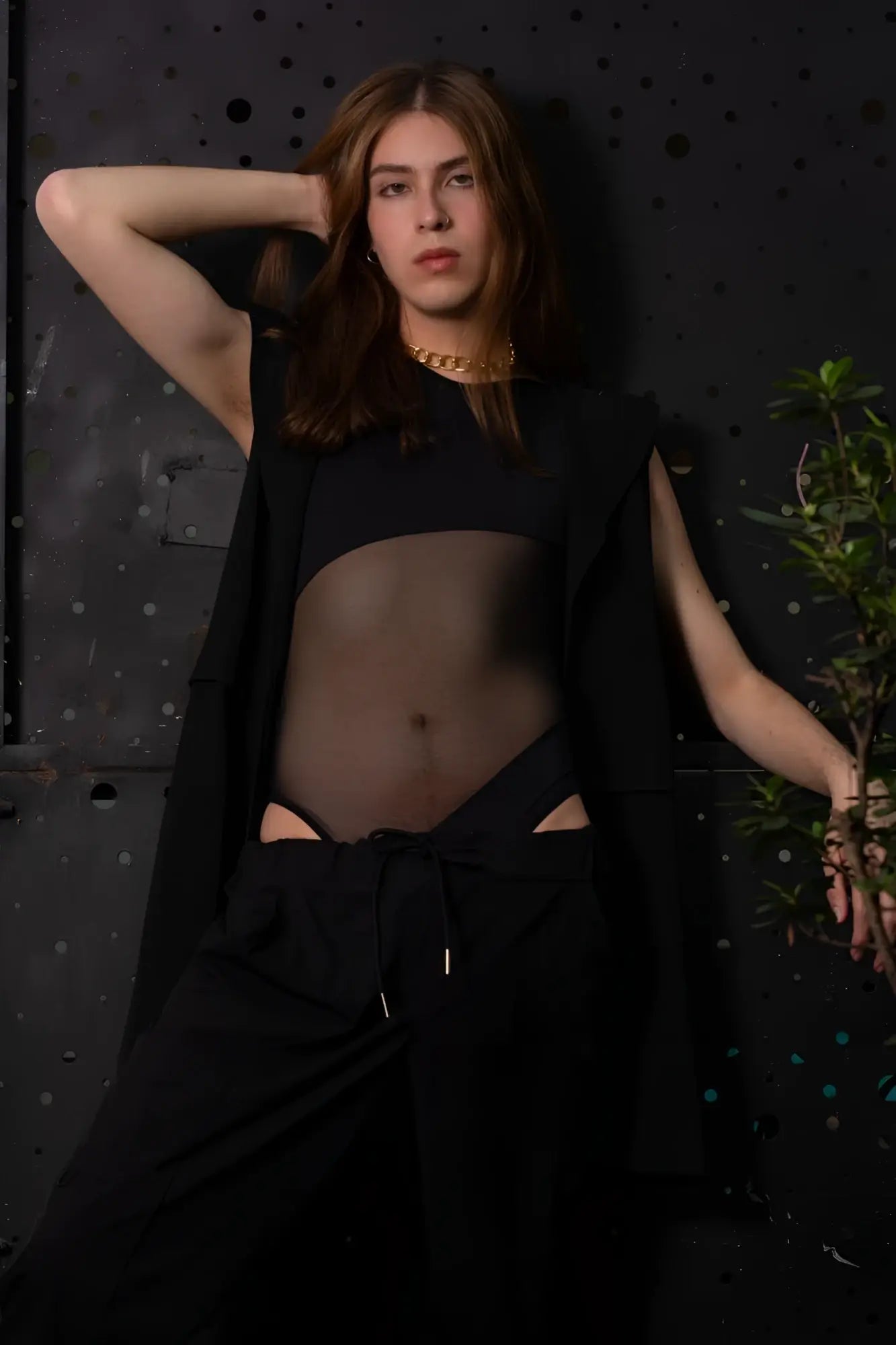 A person with long brown hair wearing a gold chain necklace with a black plural pl002 bodysuit