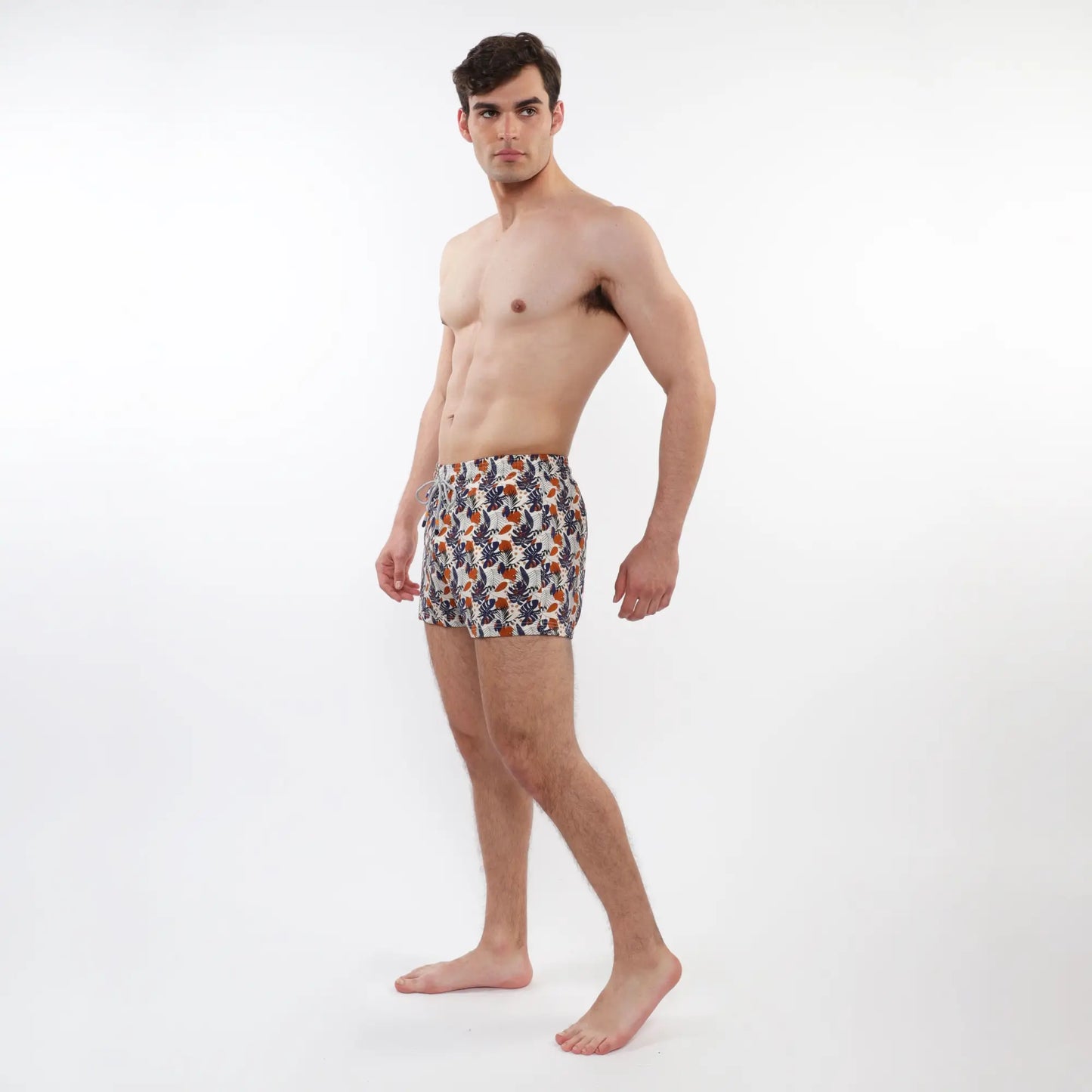 Printed swim short with mesh lining featuring vibrant tropical leaf pattern in orange navy blue and cream on white base
