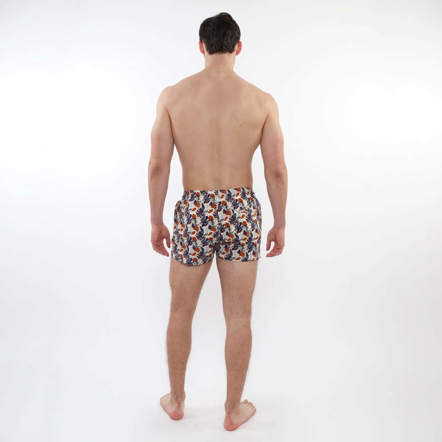 Men’s white printed swim shorts with vibrant orange and navy tropical leaf pattern and mesh lining