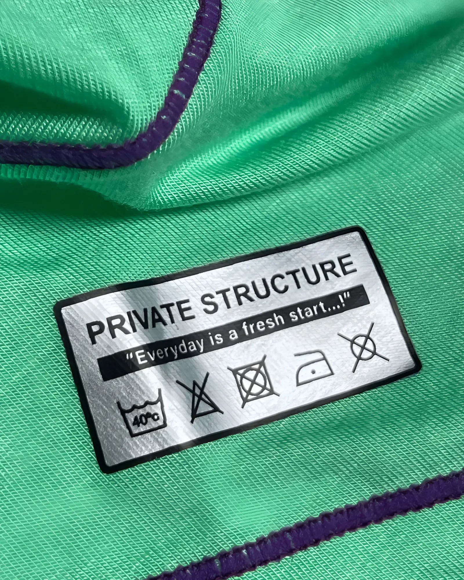 Green fabric with purple stitching and a silver private structure label showing care instructions on epus4570 hipster