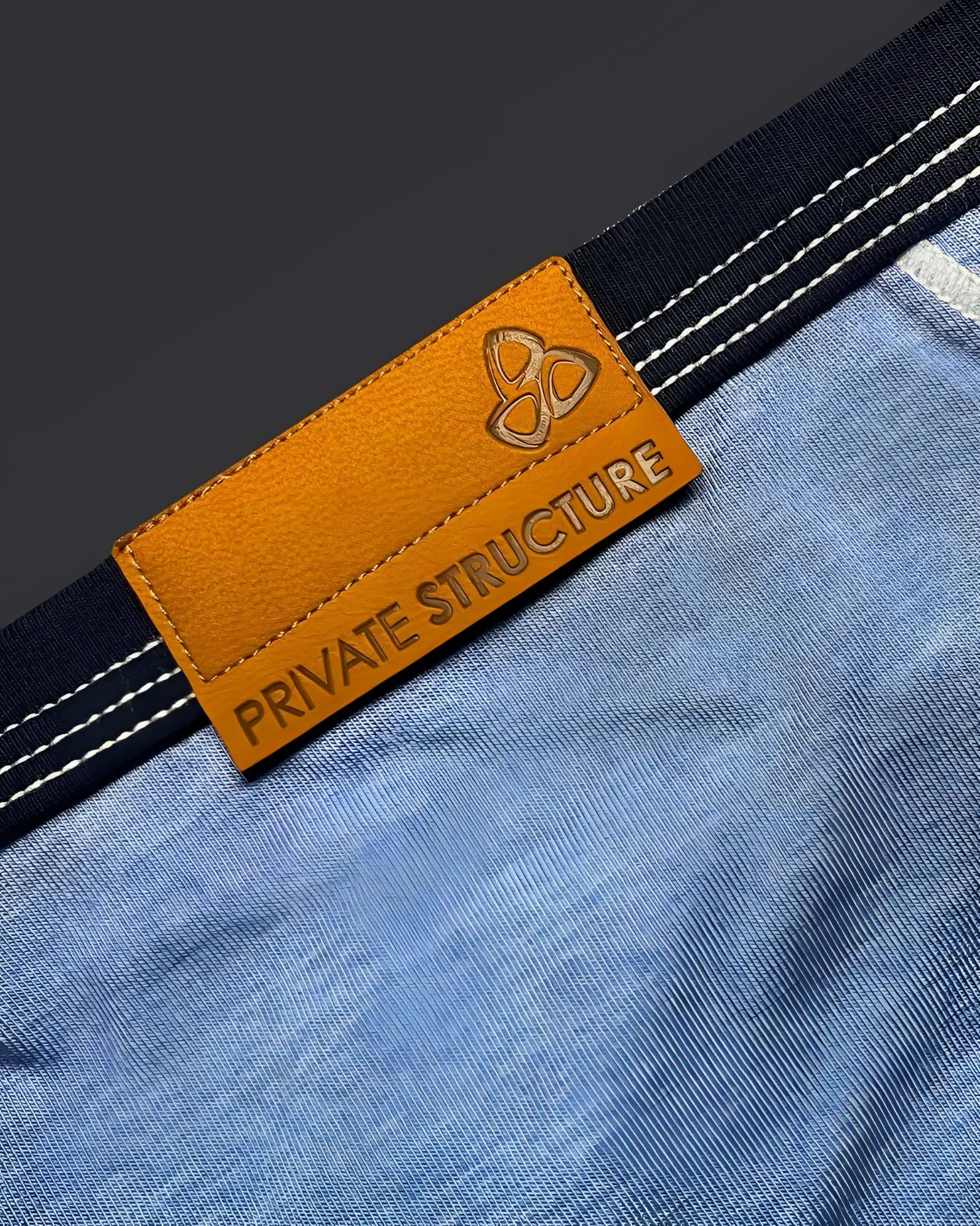 Orange leather brand tag with embossed logo and private structure text on denim fabric of low rise mini brief