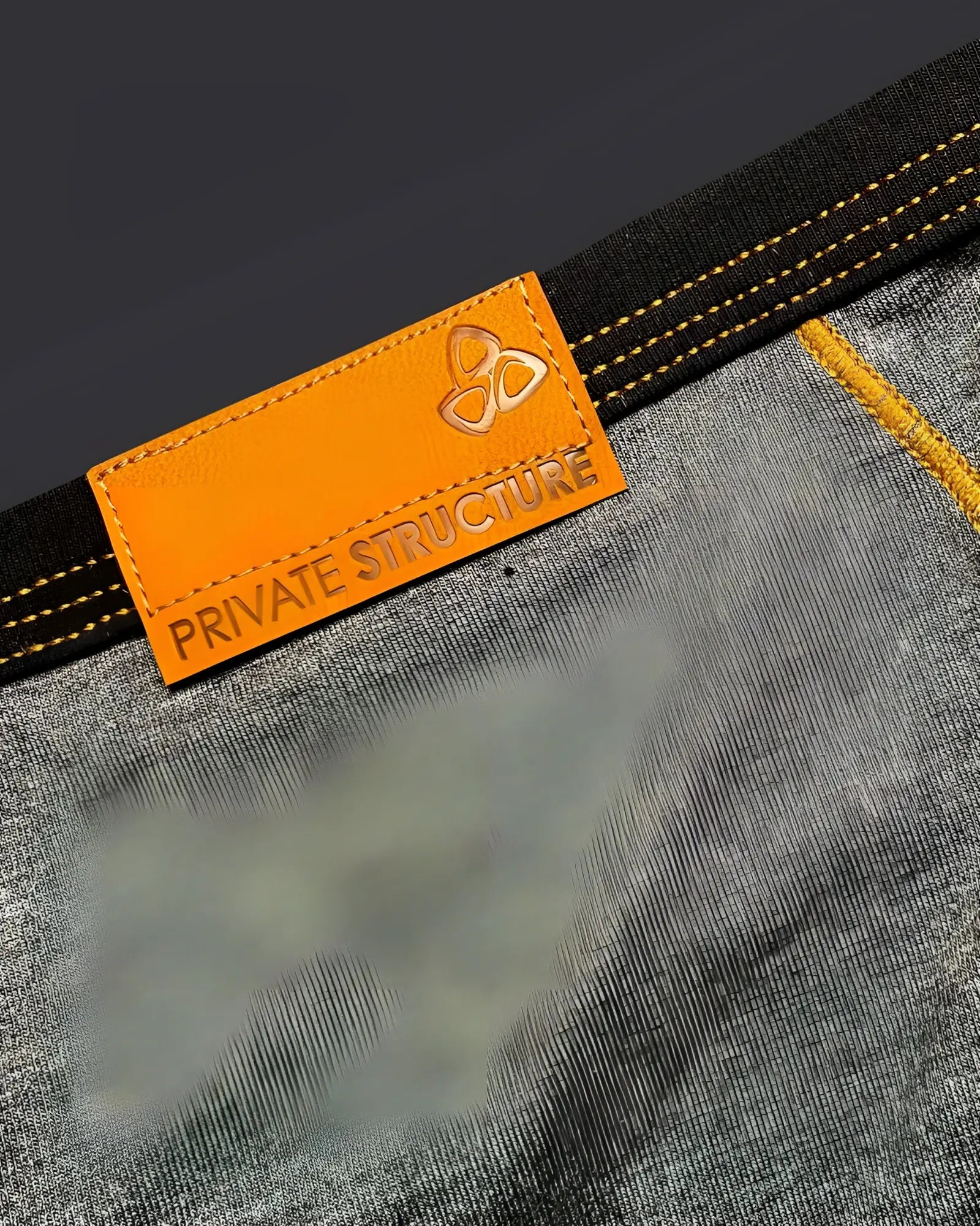 Orange leather brand tag with embossed logo and private structure text stitched on dark gray denim mini brief back