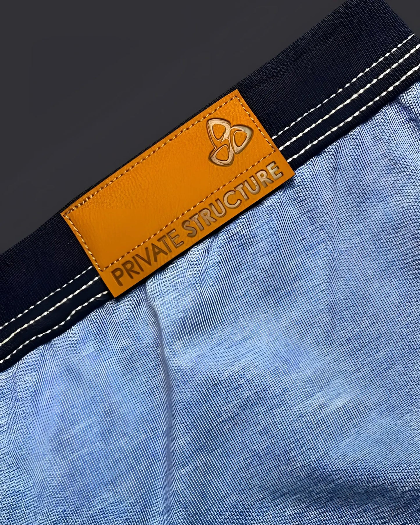 Orange leather brand tag with embossed logo and private structure text on dark blue denim waistband of barn boy low rise trunk