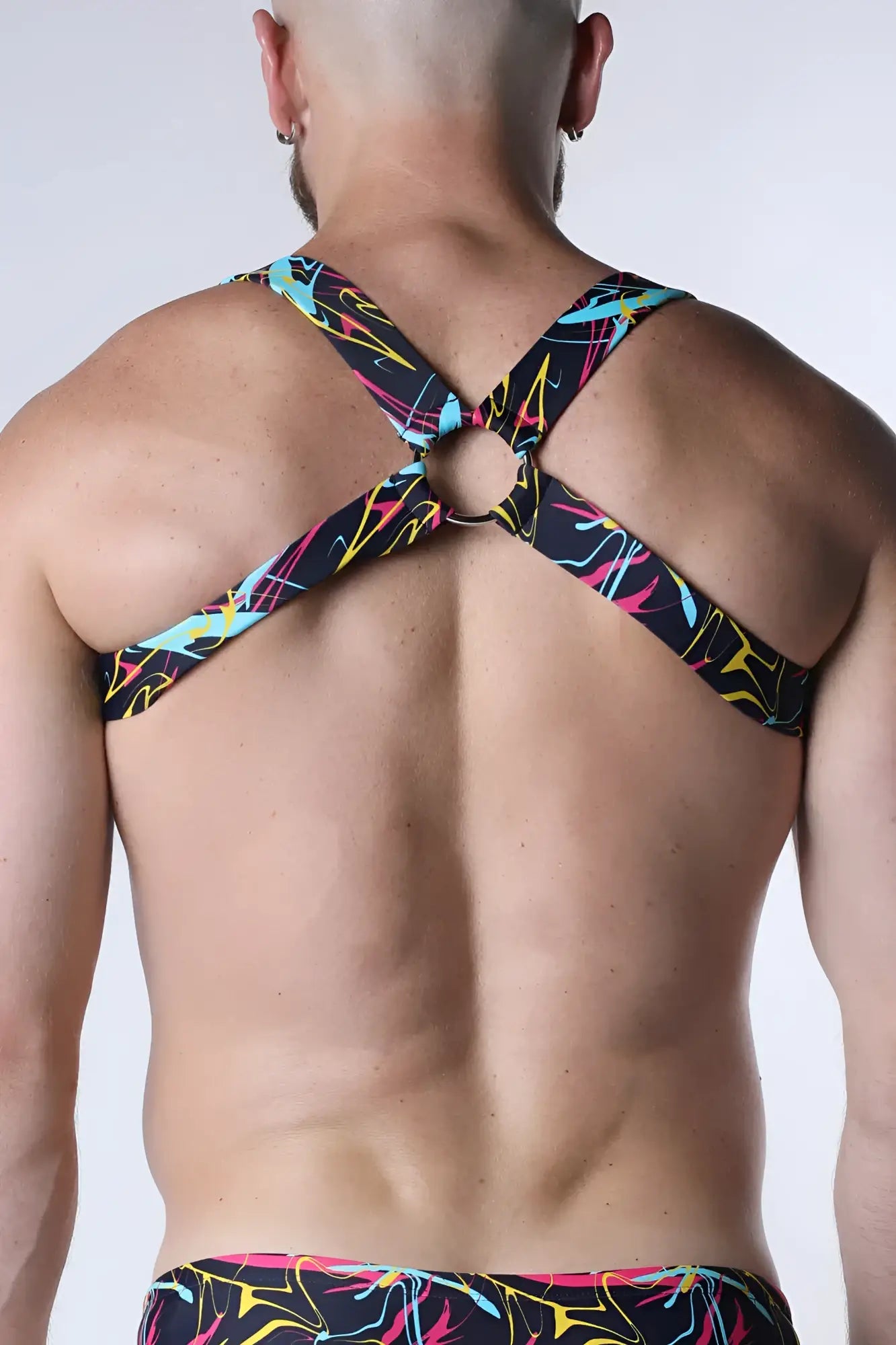 Black neon-colored abstract patterned strappy backless top with central metal ring shown from the back pulse elastic harness