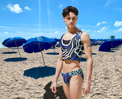 Men's crop tank top in blue and black abstract pattern made by Maris Equi worn by a model on a beach with umbrellas.