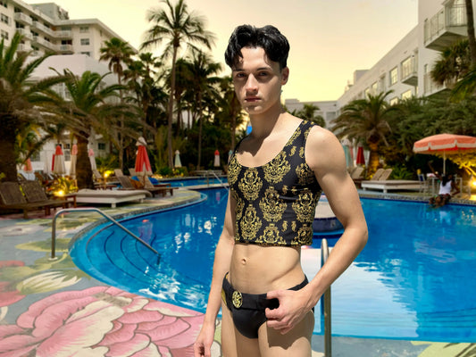 Men's black crop tank top with gold baroque pattern made by Maris Equi styled with matching swimwear by a poolside.