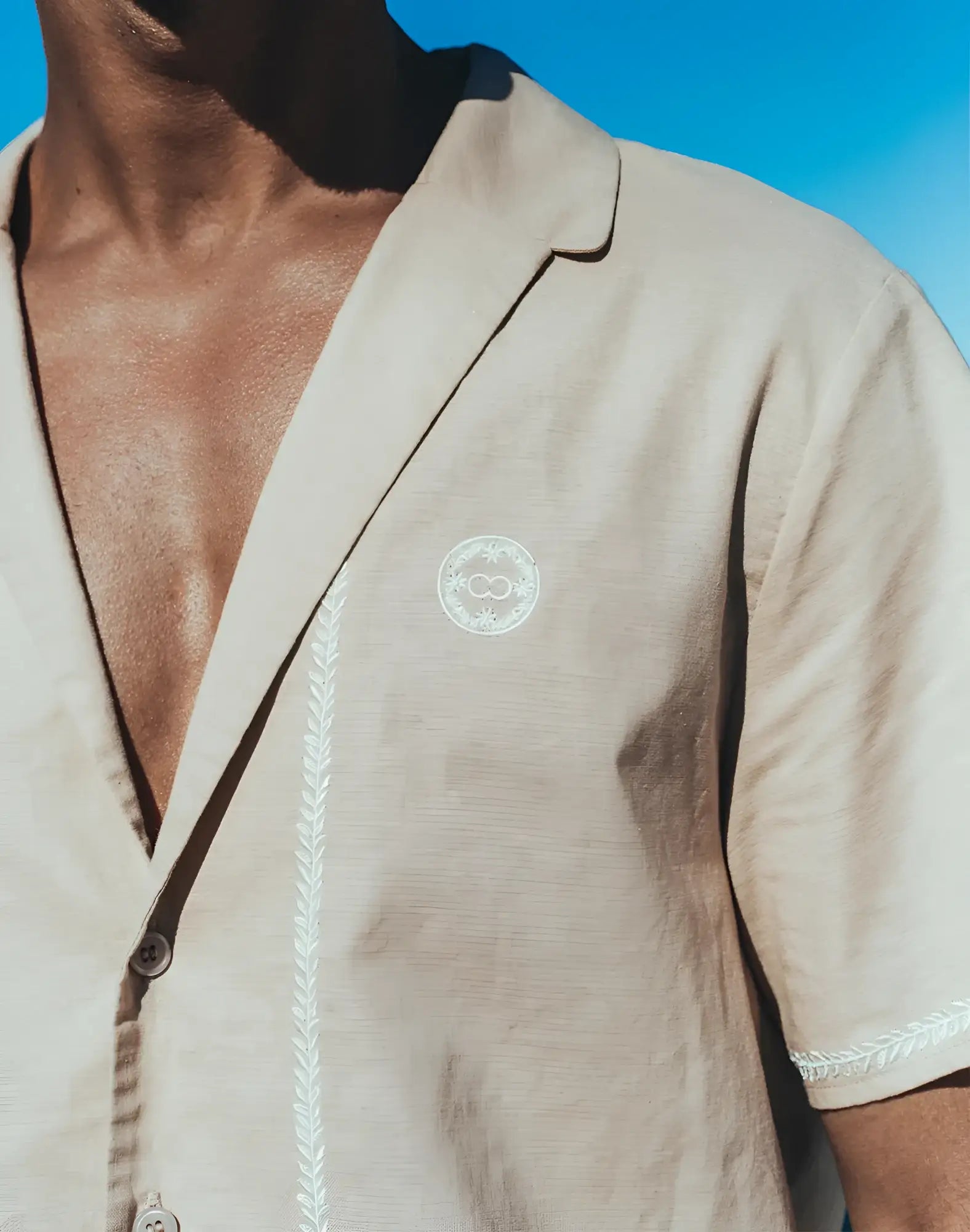 Beige linen santorini shirt with short sleeves white embroidered detailing and circular chest logo