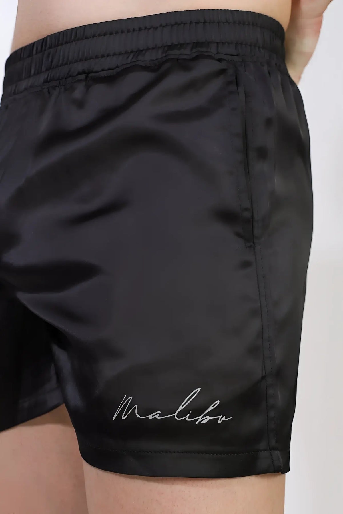 Black satin shimmerflex active shorts in midnight black with subtle sheen and malibu embroidery on lower right leg