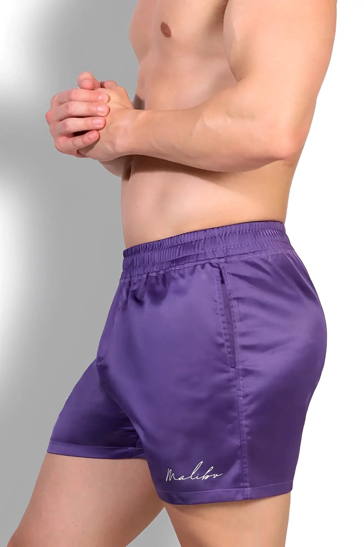 Purple satin shimmerflex active shorts with subtle malibu logo embroidered on the lower left leg