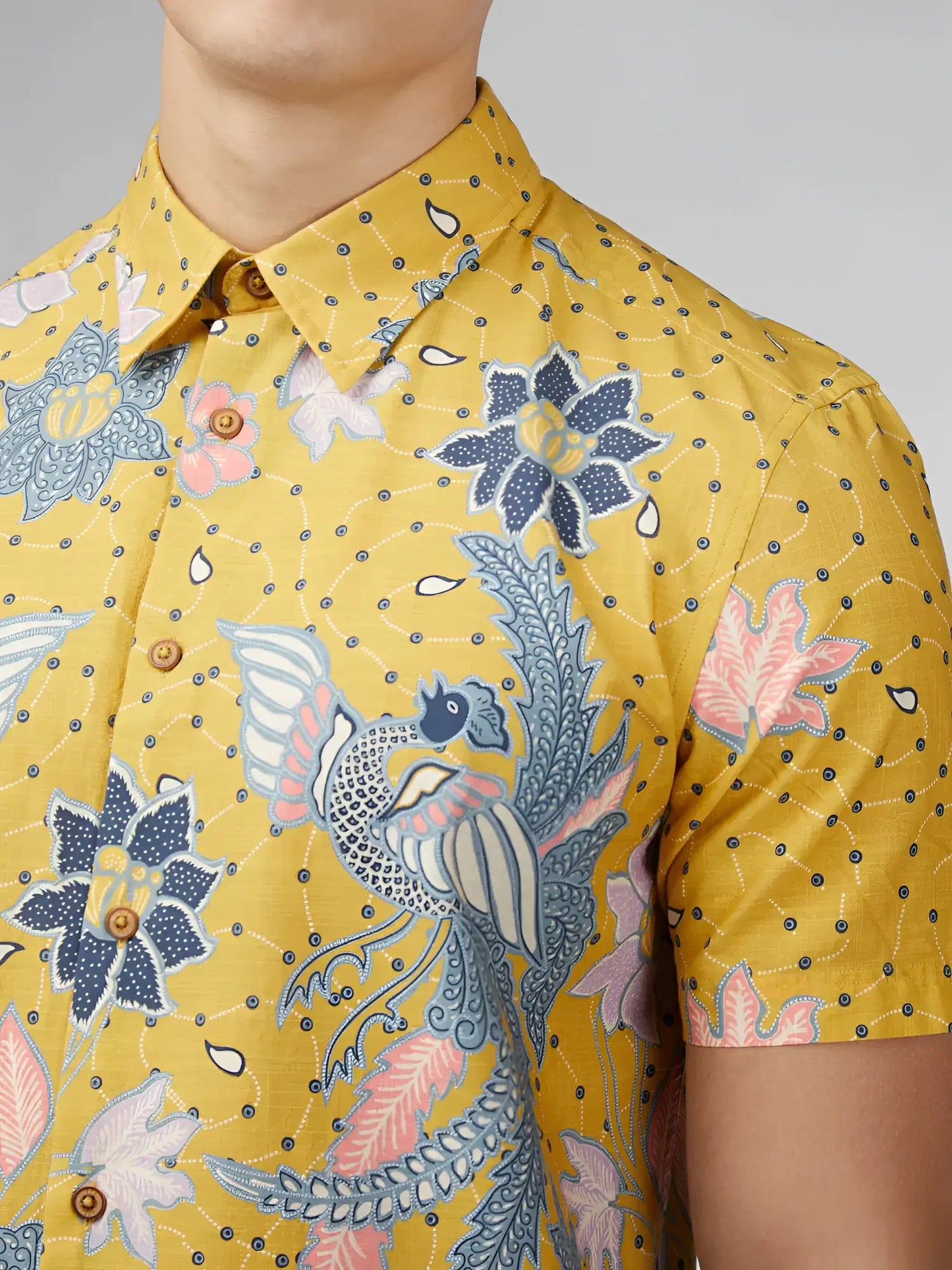 Yellow short-sleeved button-up shirt with intricate blue pink and white floral and bird patterns on textured fabric
