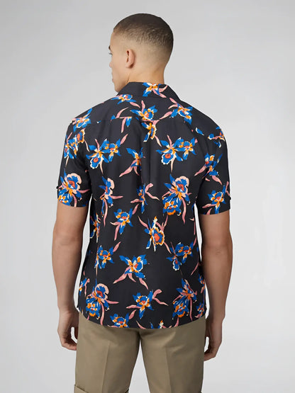 A man wearing a dark navy short-sleeved button-up shirt with vibrant blue and pink floral signature botanical print