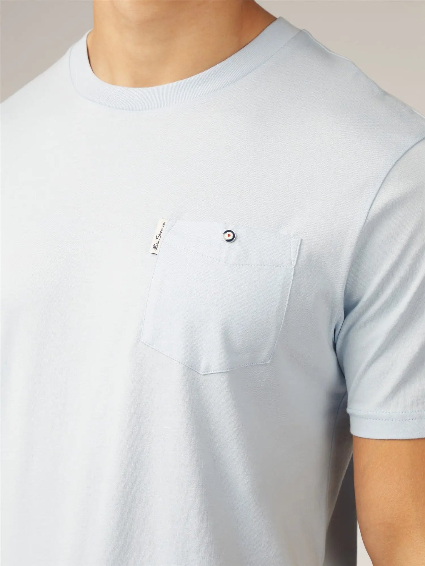 Light blue short-sleeved signature t-shirt with chest pocket and small black and white circular button closure