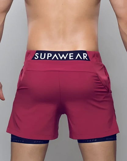 A pair of vibrant red spr max short athletic shorts with navy blue supawear logo waistband and matching compression shorts