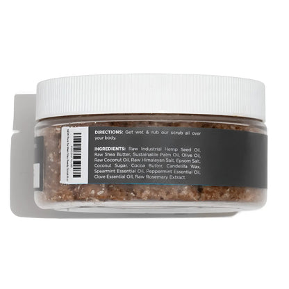 A clear plastic jar with white ribbed lid contains brown granular body scrub stay ready scrub with ingredient label