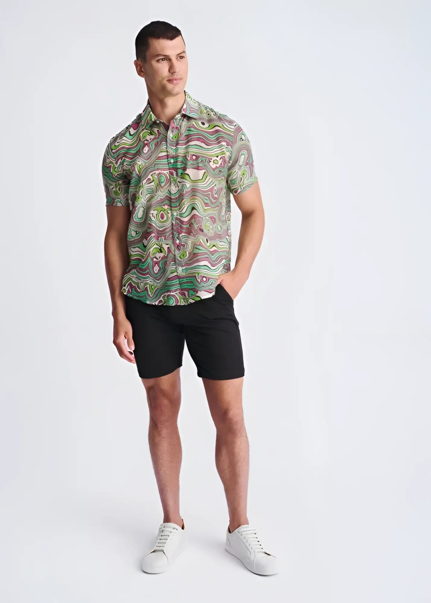 A man wearing a swirls lightweight cotton silk short-sleeved shirt with green pink and beige abstract patterns