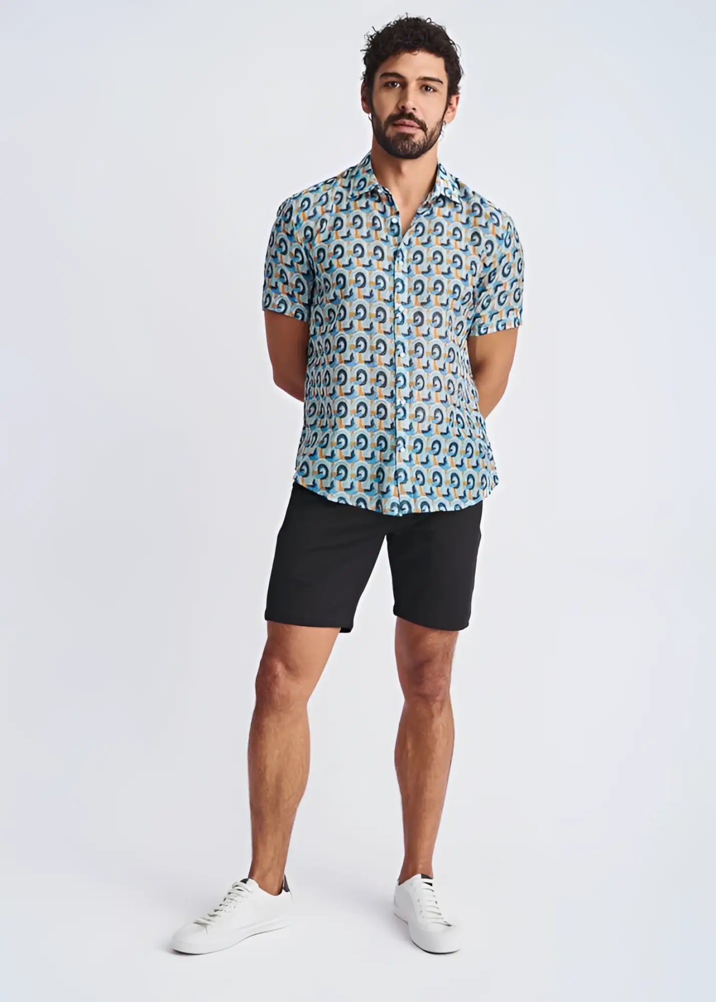 A man wearing a swirls lightweight cotton silk short sleeve shirt with blue green and yellow circular patterns on light teal