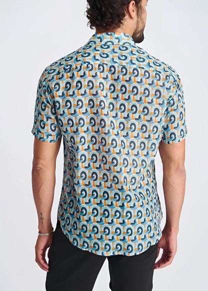 A man wearing a swirls lightweight cotton silk short-sleeved shirt with blue and orange geometric patterns on turquoise