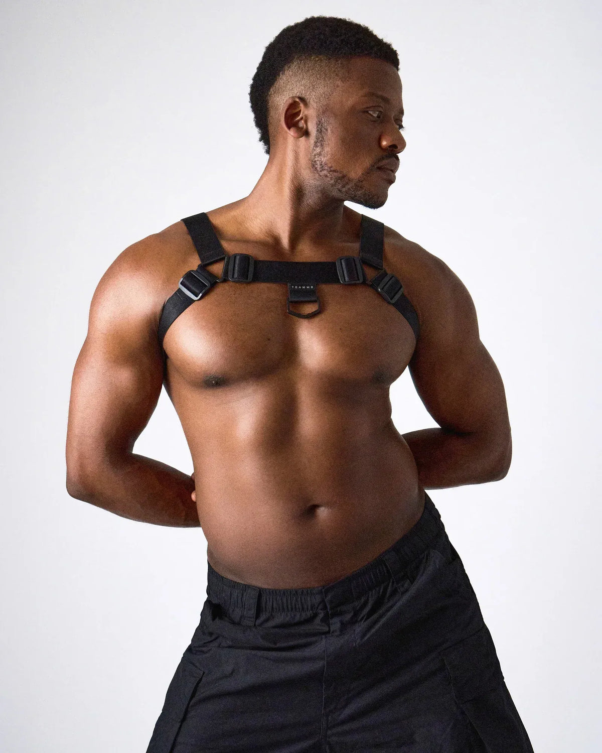 A model wearing a black harness with adjustable straps and a central ring showcasing a muscular physique by teamm8