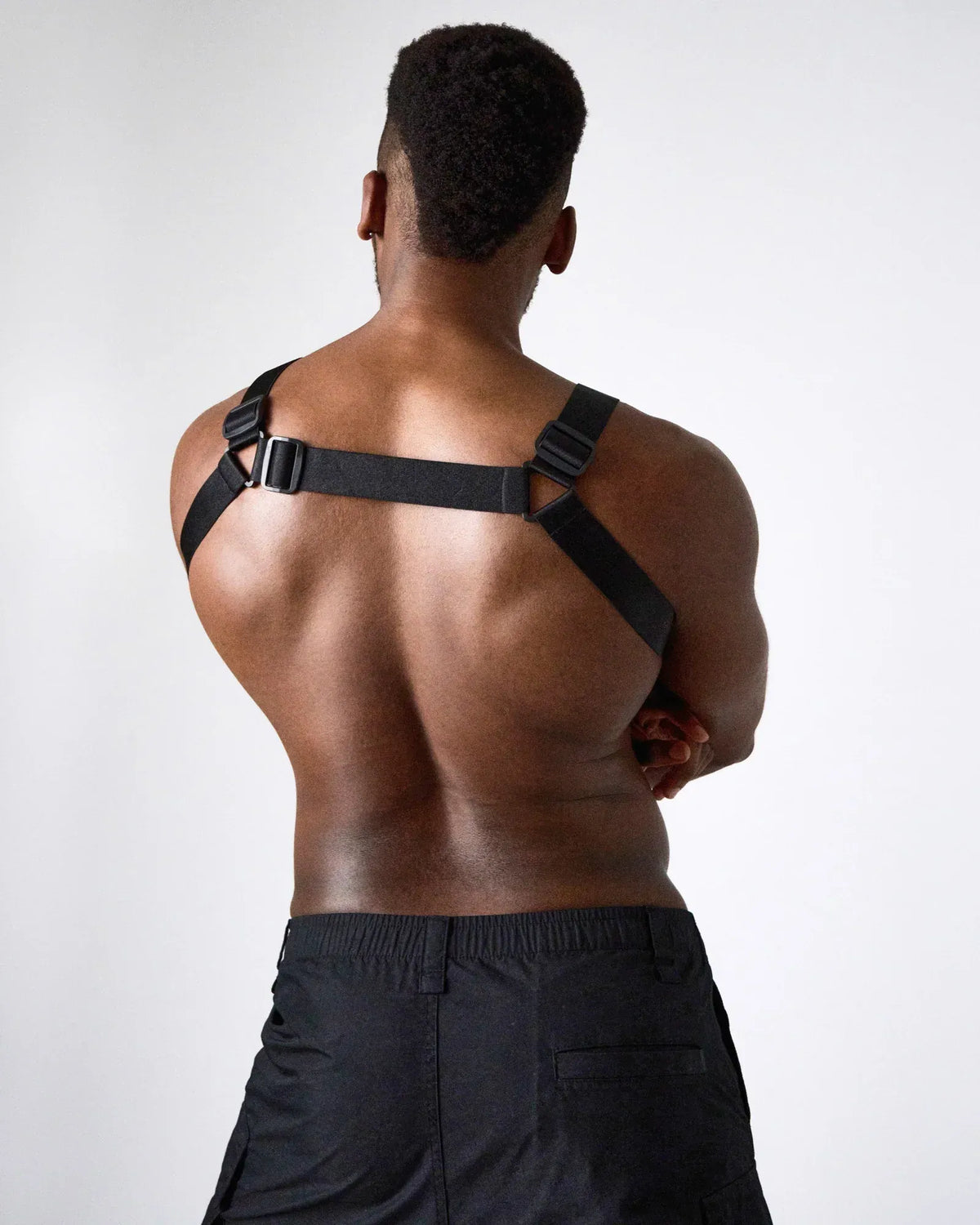 A model wearing a black harness with adjustable straps showcasing a muscular back styled with black shorts by teamm8