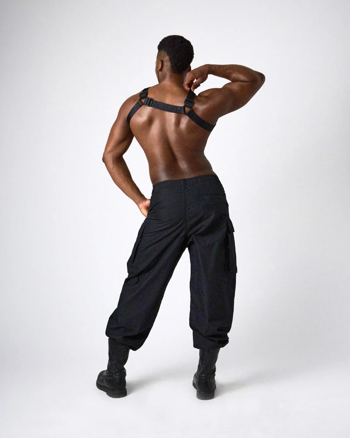 A model wearing a black harness with adjustable straps paired with loose black cargo pants and black boots showcasing a stylish look by teamm8