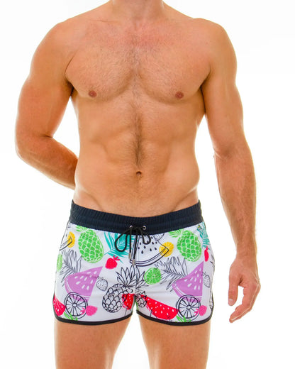White swim trunks with vibrant tropical fruit print featuring pineapples watermelons and strawberries in multiple colors