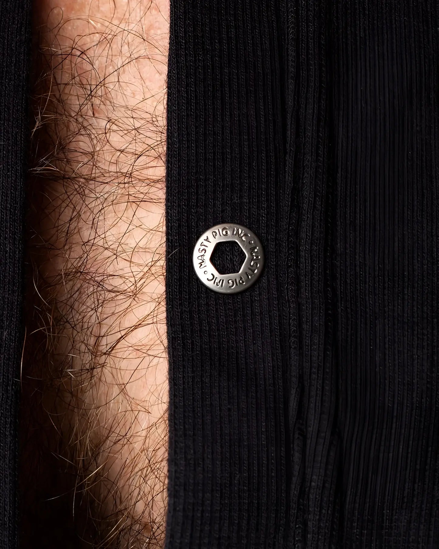 Union suit featuring a silver-toned hexagonal snap button engraved with musty pig inc on black ribbed fabric
