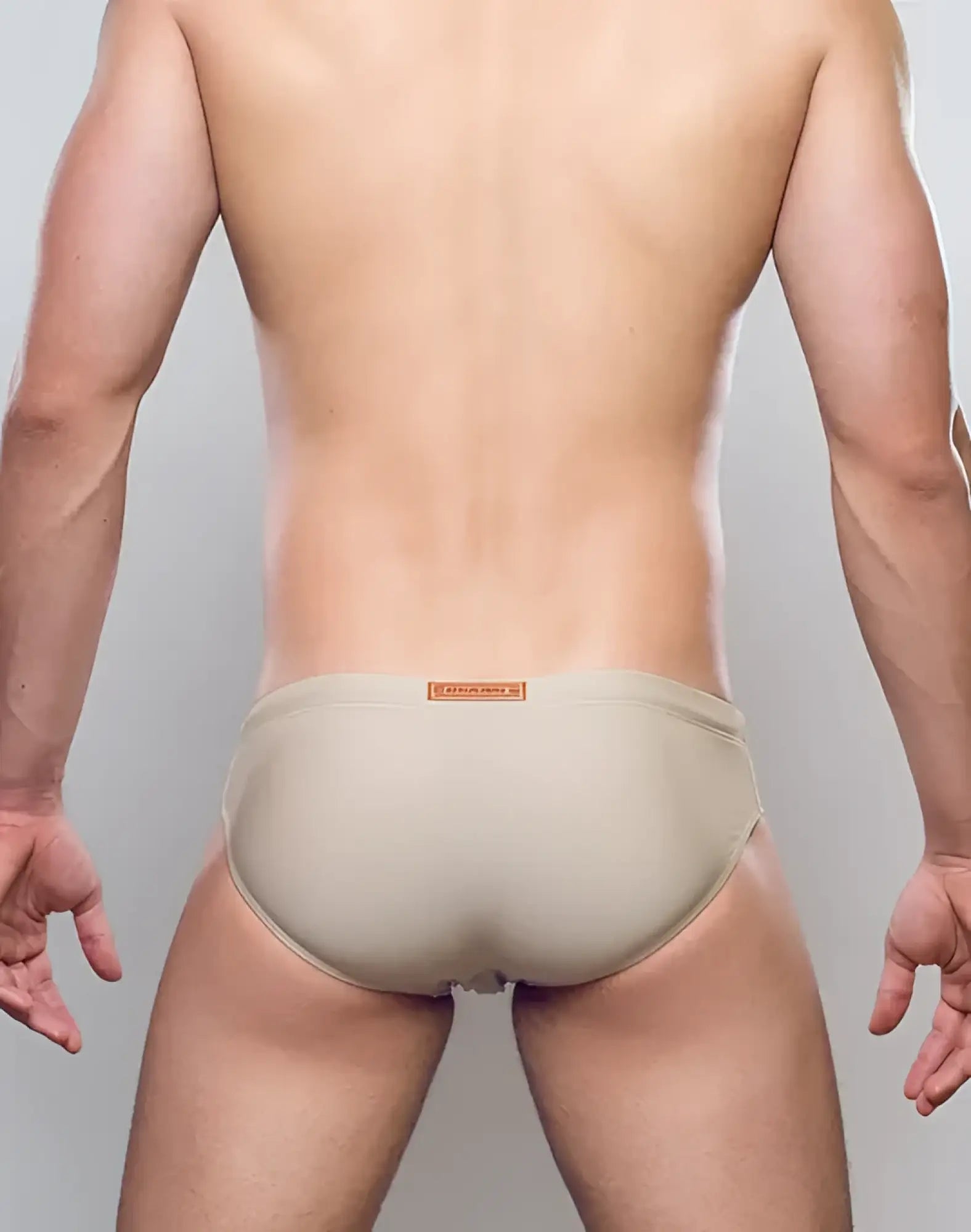 Beige form-fitting v10 core bikini swim trunks with a subtle orange brand tag at the waistband