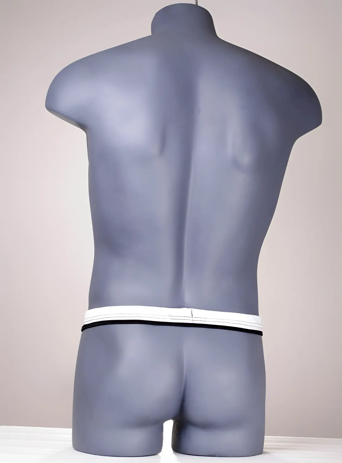 White and black thong on a grey male mannequin torso, showing the slim waistband from the back.